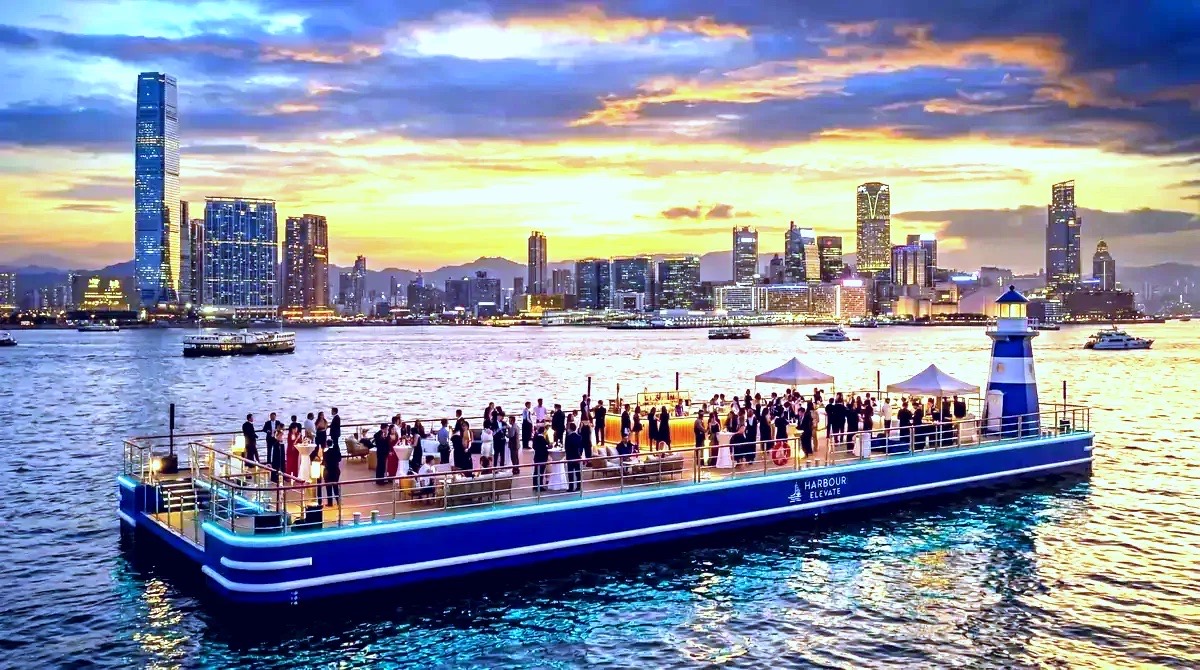 Event barge with guests gathered on deck at sunset, with a city skyline behind