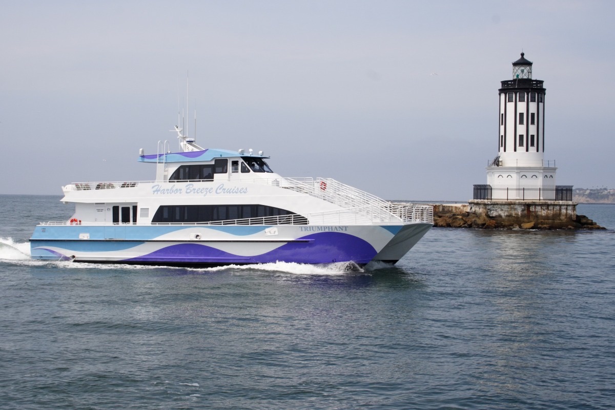 Passenger catamaran cruising past a harbor lighthouse